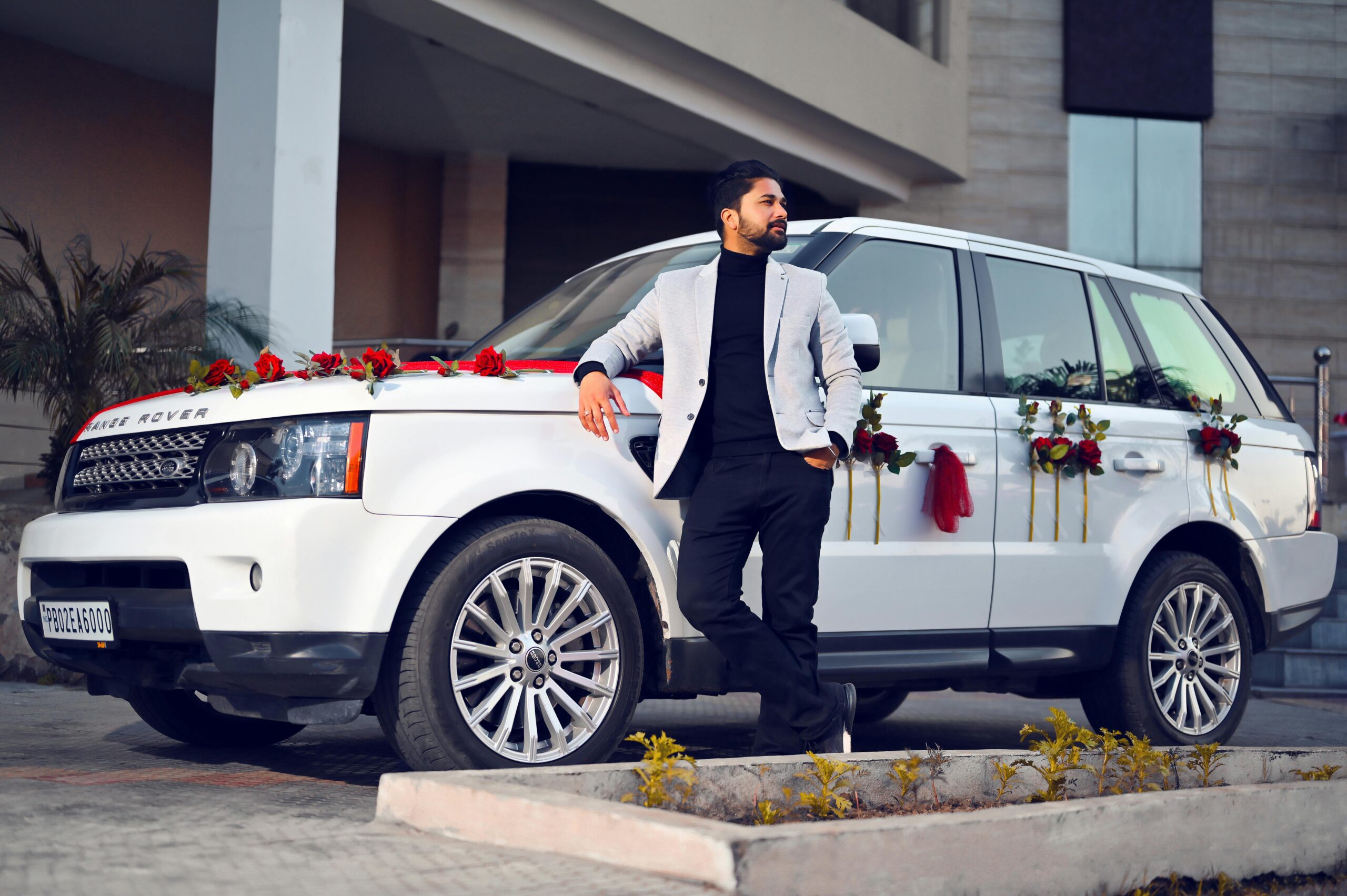 Fashionable man in a blazer leaning on a flower-adorned Range Rover in Amritsar.