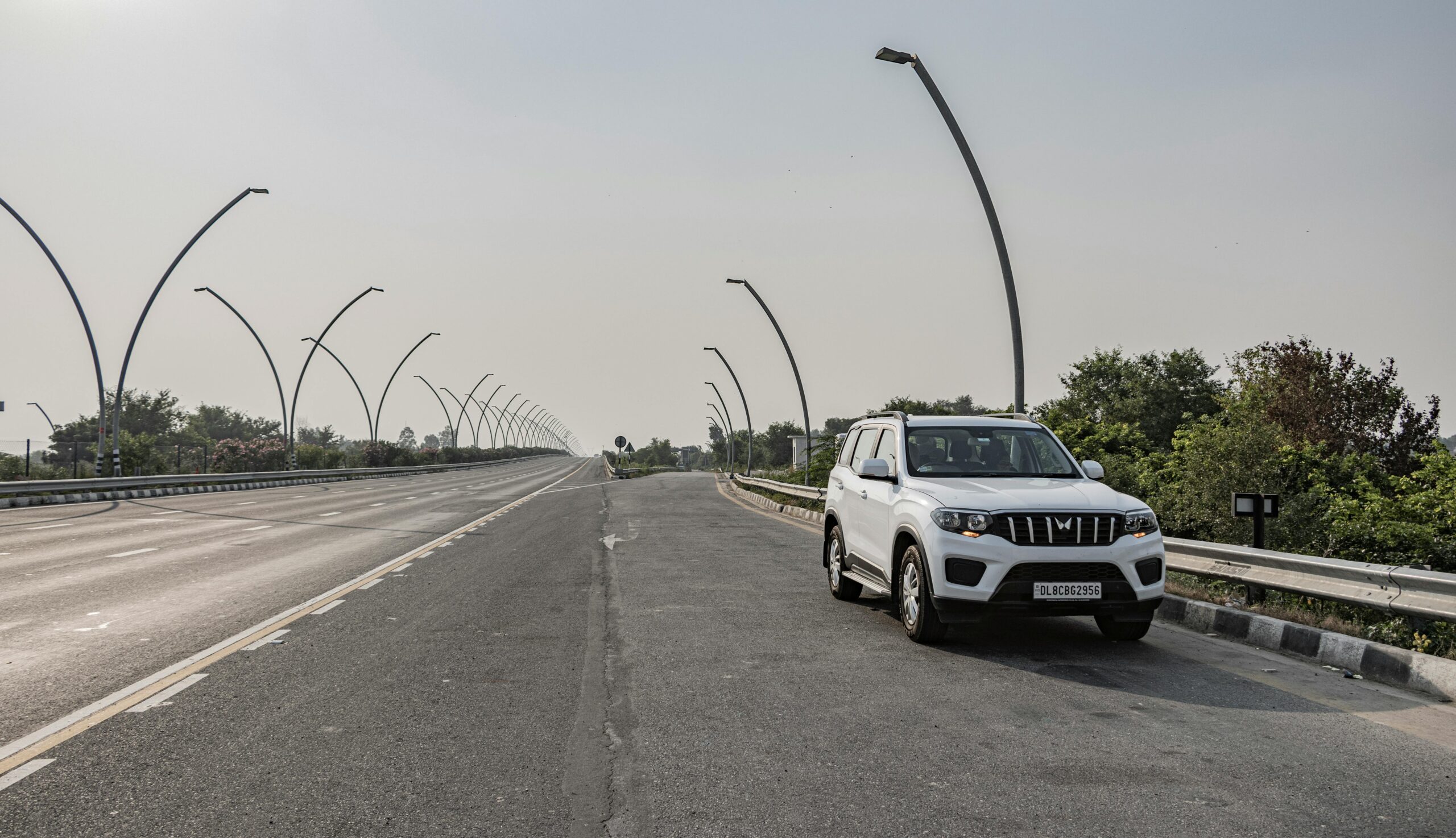A white SUV parked on an expressway near Deeg, Uttar Pradesh, India under clear skies.